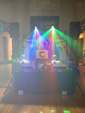 DJ setup with colorful stage lights, speakers, and a table with equipment, in a room.
