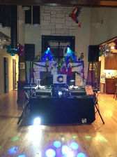 DJ setup with turntables, lights, and speakers in a room with a fireplace and wood floor.