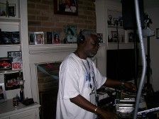DJ playing music at a home party. Man in white shirt, brick fireplace background.