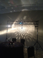 A spotlight shines patterns on a wall behind a table with chairs; lights are mounted on a stand.