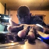 Man with a shaved head reaching toward the camera with outstretched hand. Dimly lit setting.