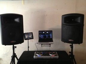 DJ setup with two black speakers on stands, a laptop, and a mixer on a table.