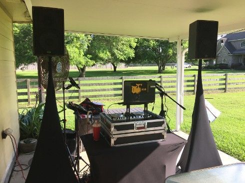 DJ setup on a patio with speakers, mixer, and microphone, facing a grassy yard.