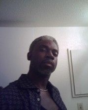 A man with graying hair and a goatee poses indoors, wearing a dark patterned shirt.