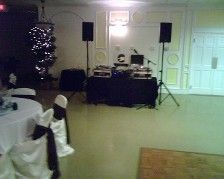 DJ setup with speakers, table, and microphone in a room with tables and chairs set for a party.