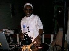 DJ at outdoor event, wearing white, spinning records.