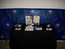 Table with black cloth, items for sale, against blue star backdrop.