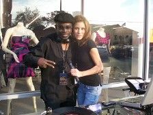 A DJ and woman pose at a window display. The DJ gives peace sign, next to a woman holding a microphone.