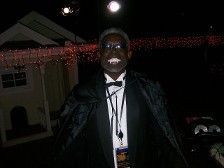 Person in a vampire costume, smiling, wearing a black cape and bowtie, at a Halloween event.