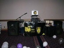 DJ setup with speakers, microphone, laptop, and balloons, in a room with a dark carpet.