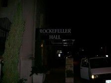Rockefeller Hall sign lit up at night, with a vehicle parked in front.