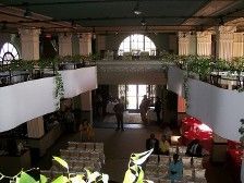 Large event space with tables, balconies, and a raised entryway. Sunlight streams in.