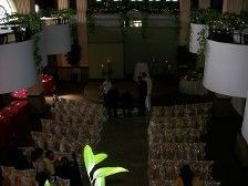 Wedding ceremony setup with clear chairs, overhead lamps, and greenery.