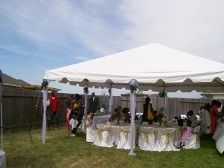 Outdoor event tent with people; tables with gold linens, cloudy sky.