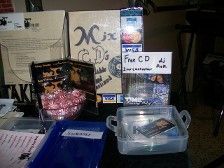 A table displays a free CD giveaway: boxes, CDs, a candy bowl, and sign that says 