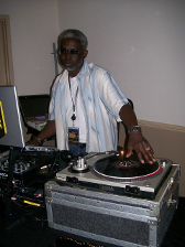 DJ spinning records, wearing a light blue shirt, at an event.