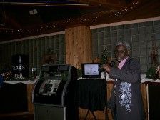 Man in suit singing at a venue, holding a microphone.  Jukebox and screen in background.