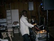 DJ wearing a white shirt, playing records at a dimly lit event.