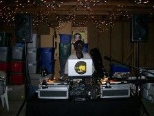 DJ at a basement party with turntables and laptop. Speakers flank the setup.