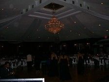 Inside a ballroom with a chandelier and a high ceiling, wedding party walking on a dance floor.