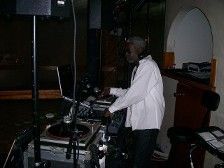 DJ in a white shirt and headphones mixing music on turntables in a dimly lit venue.