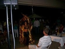 A belly dancer in gold costume performs at an outdoor party at night, with people watching.