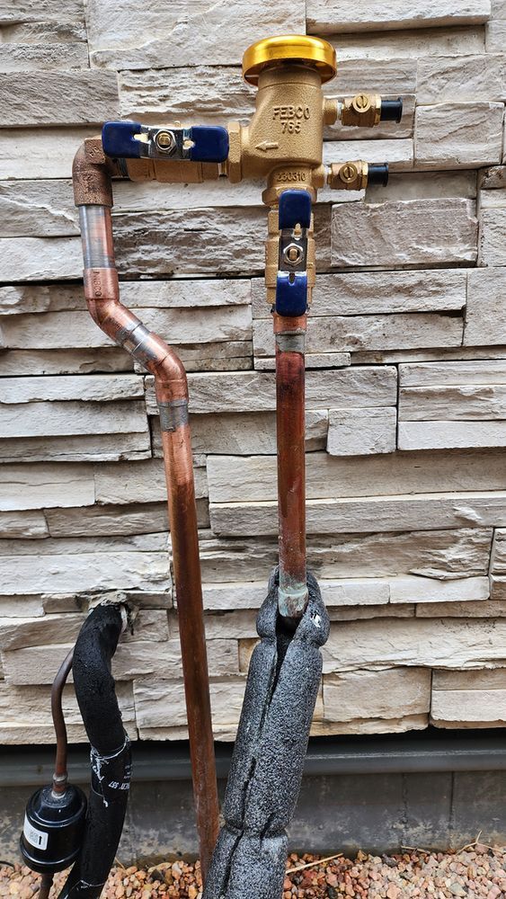 A copper pipe with a valve attached to it is sitting in front of a brick wall.