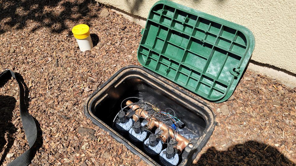 A sprinkler box is sitting on the ground next to a yellow bottle.