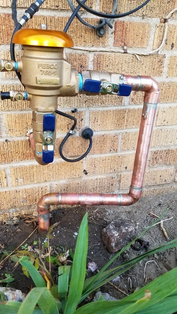 A copper pipe is attached to a brick wall next to a plant.