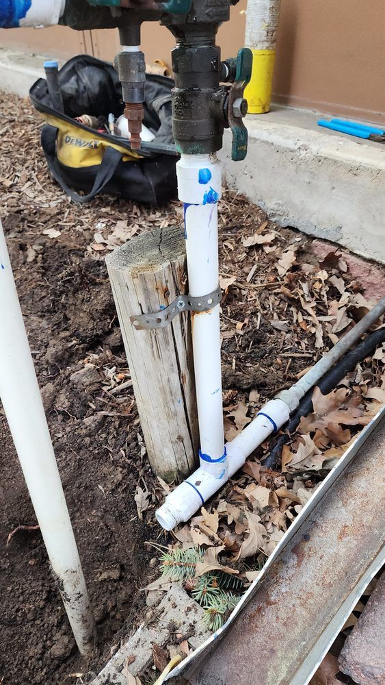A white pipe is sitting next to a wooden post in the dirt.