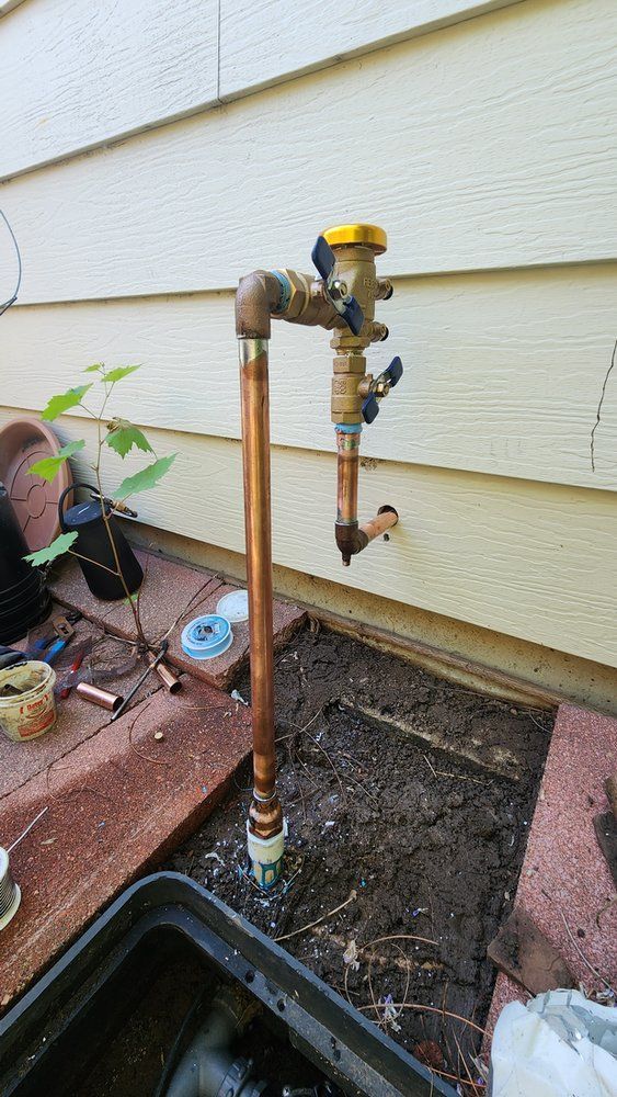A copper pipe is sitting in the dirt next to a house.