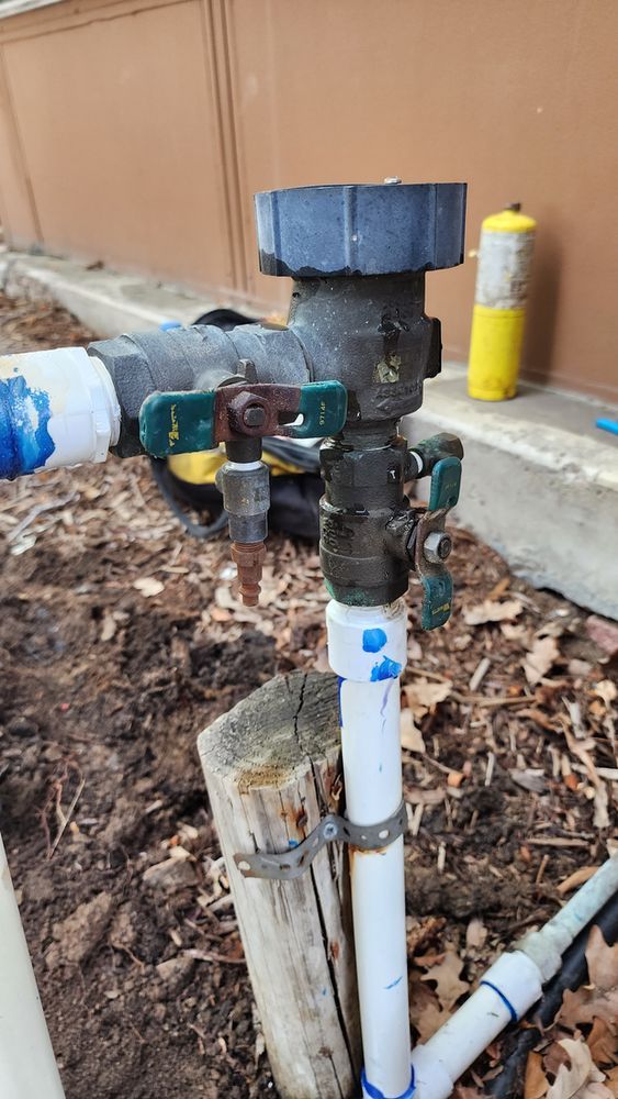 A water sprinkler is sitting on top of a wooden post next to a pipe.