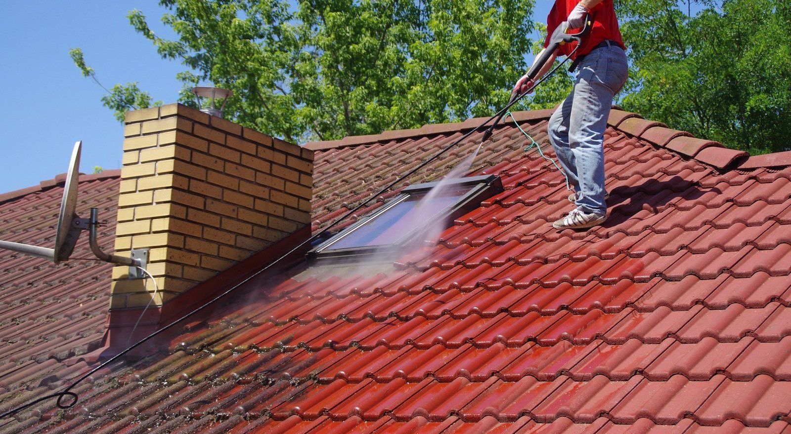 A man is cleaning the roof of a house with a high pressure washer.