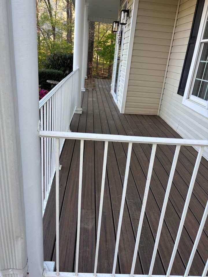 Narrow wooden porch with white railings and beige siding, viewed through an open gate.