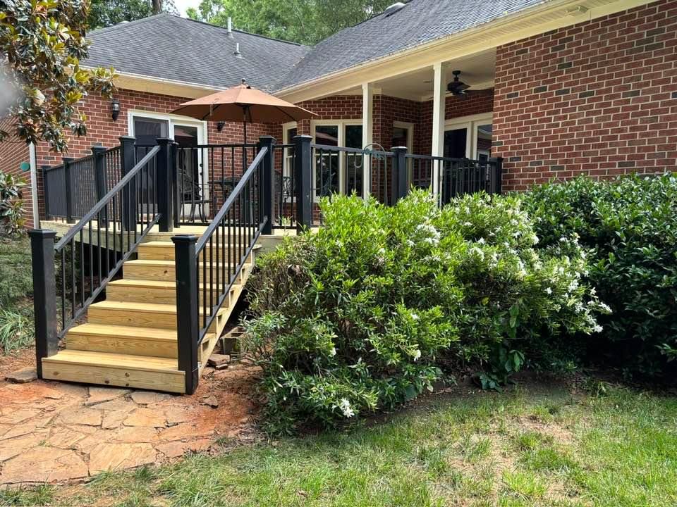 Brick house front porch with black railings, steps, and green shrubs in the yard