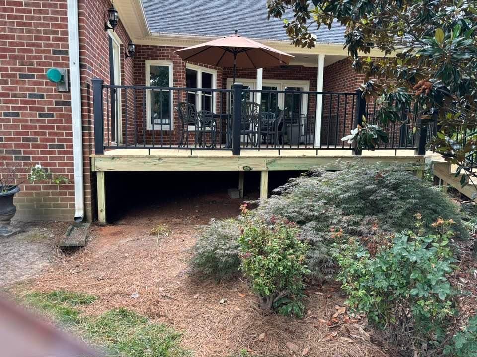 Brick house porch with black railings and stairs above a landscaped front yard