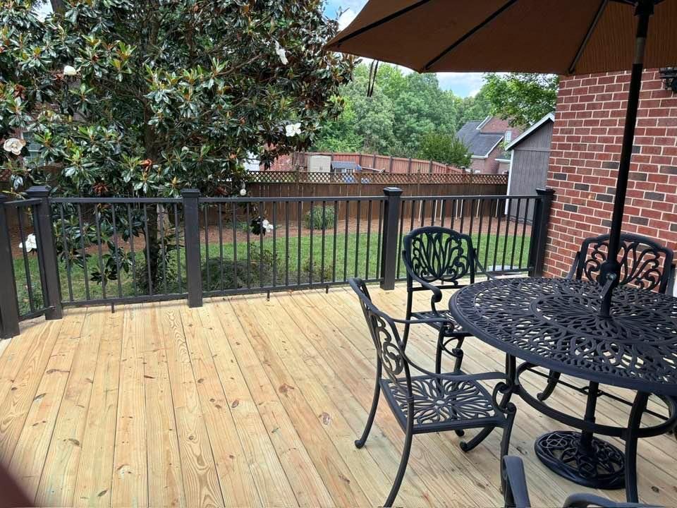 Wooden backyard deck with black metal table and chairs under an umbrella, overlooking a fenced yard.