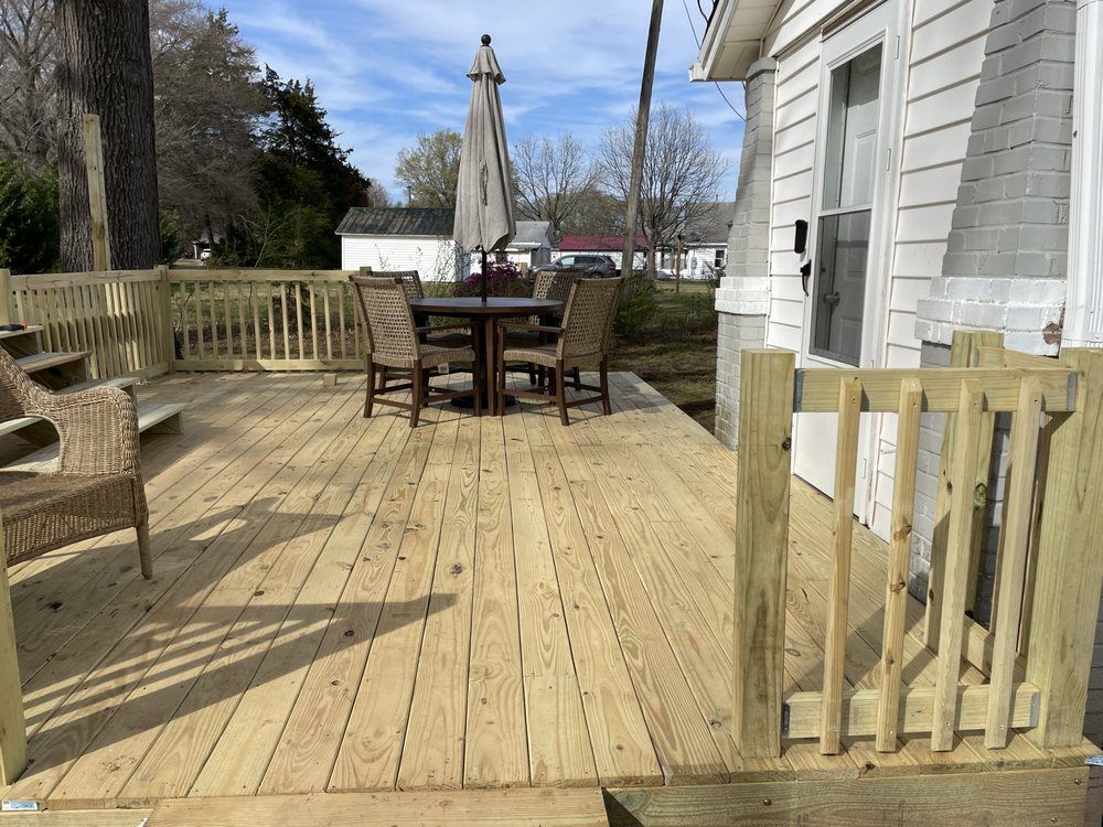 Wooden backyard deck with patio table, umbrella, chairs, and a white house beside a railing gate