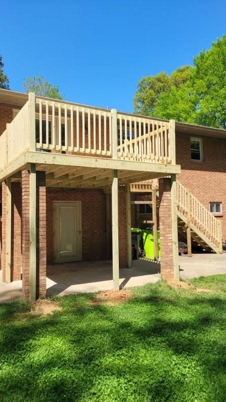 Brick apartment exterior with a raised wooden deck and stairs; a worker in a neon vest stands below.