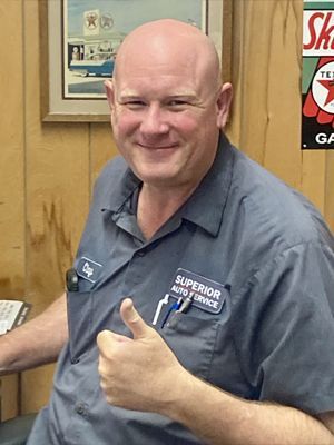 Smiling man in gray work shirt giving a thumbs-up in an office setting