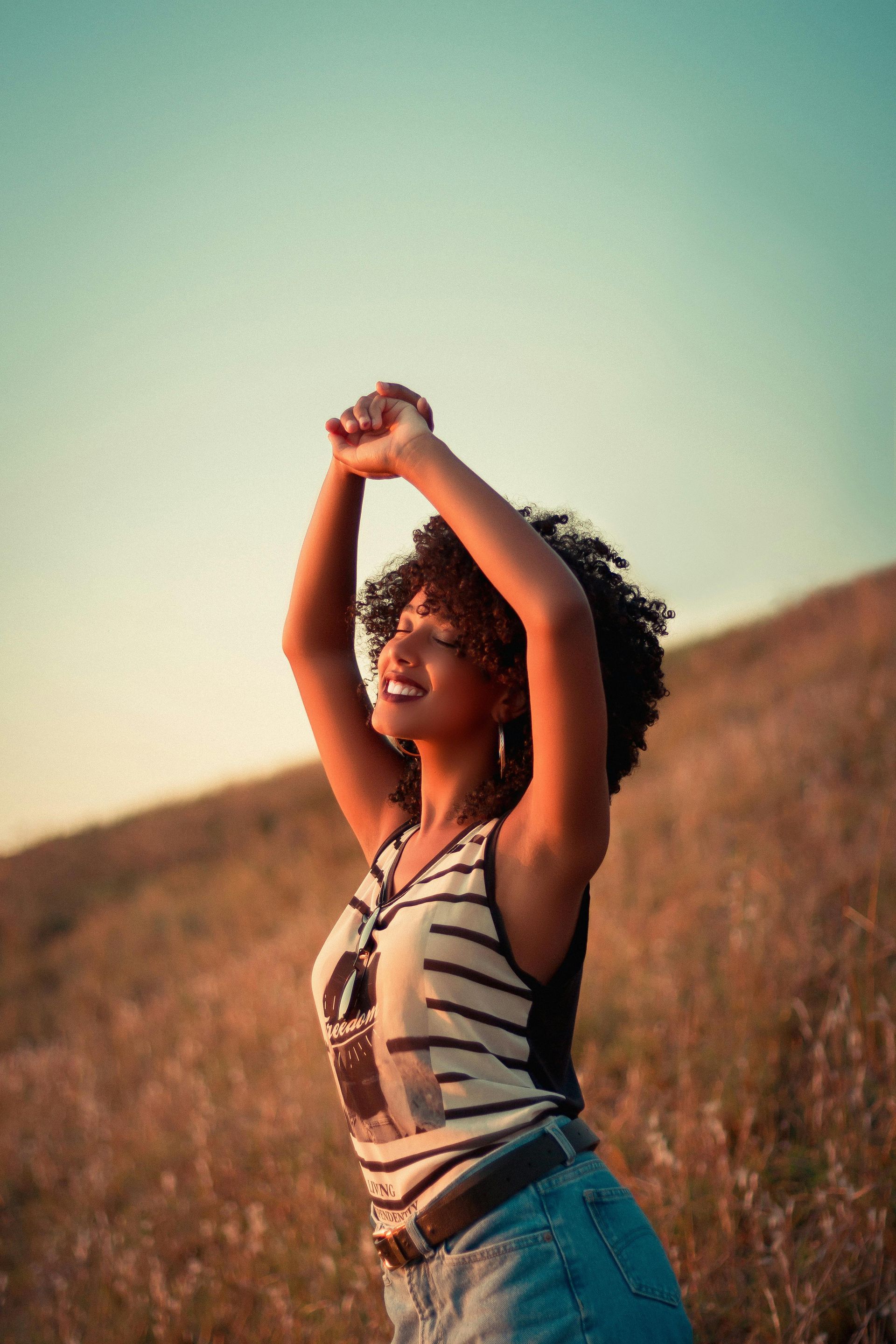 Personne s'étirant, les bras levés, dans un champ herbeux baigné de soleil au coucher du soleil.