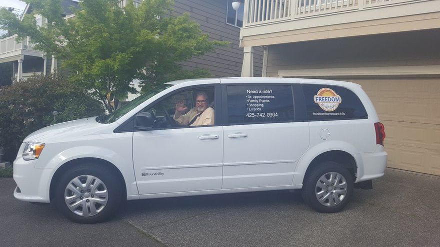 White minivan with two people inside; parked in front of a house, windows with business advertising.