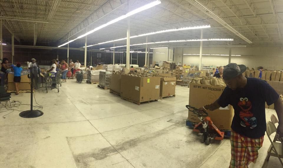 A man is pushing a pallet truck in a large warehouse filled with boxes.