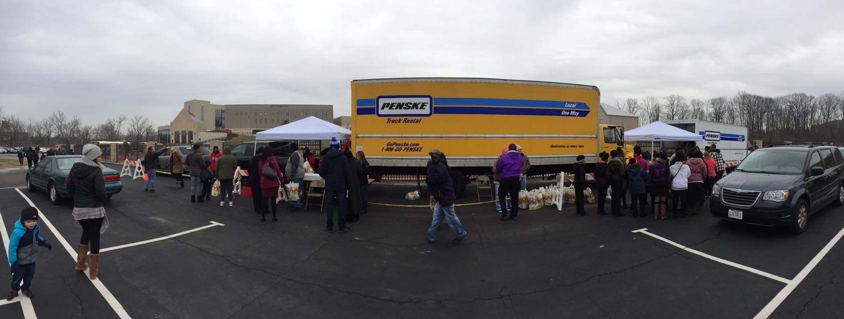 A group of people are standing in a parking lot in front of a large yellow truck.