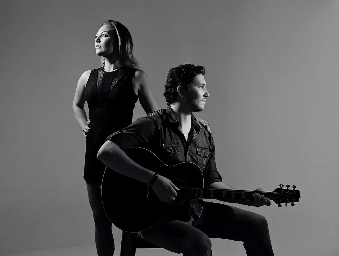 A man and a woman are standing next to each other holding guitars.
