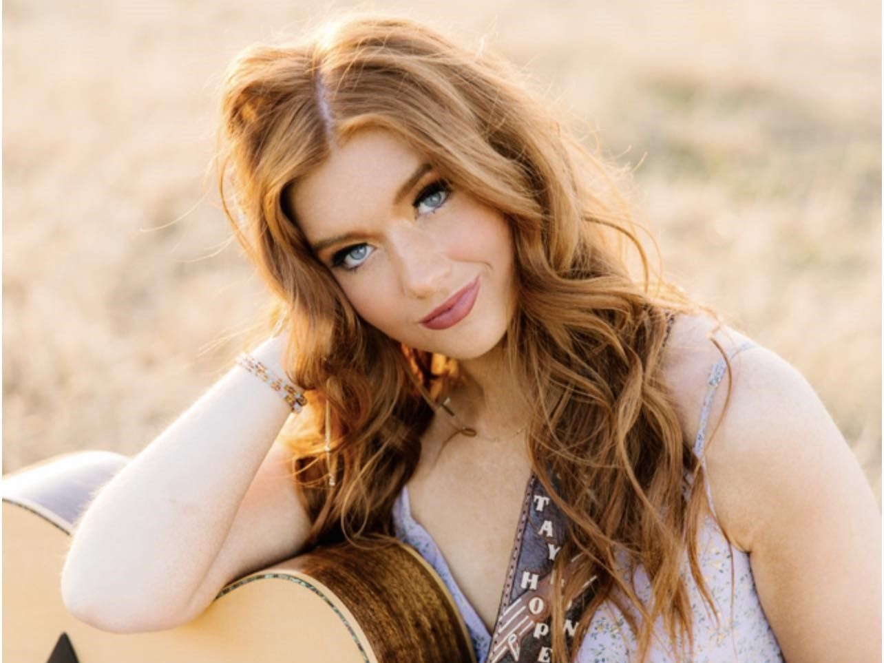 A woman is leaning on a guitar in a field.