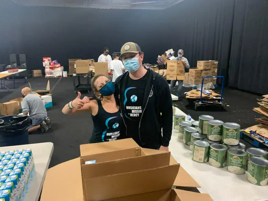 A man and a woman are standing next to each other in a room filled with boxes and cans.