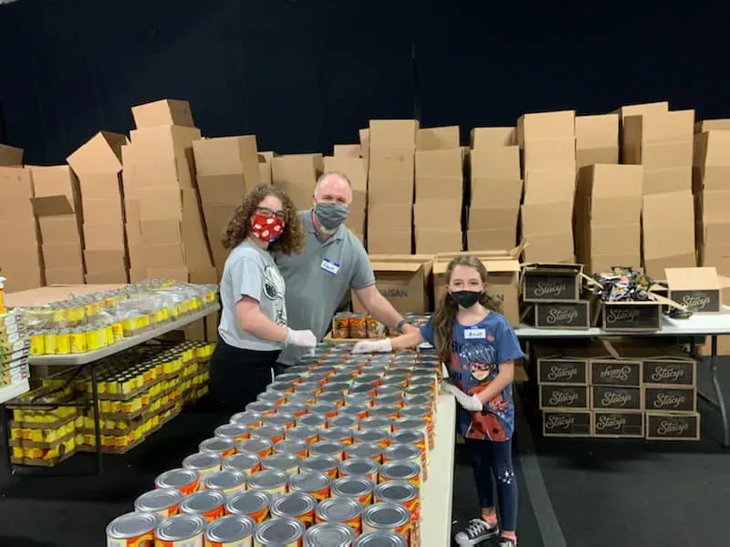 A group of people are standing around a table filled with cans of food.