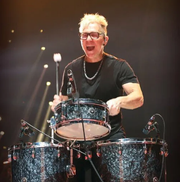 A man wearing glasses is playing drums on a stage