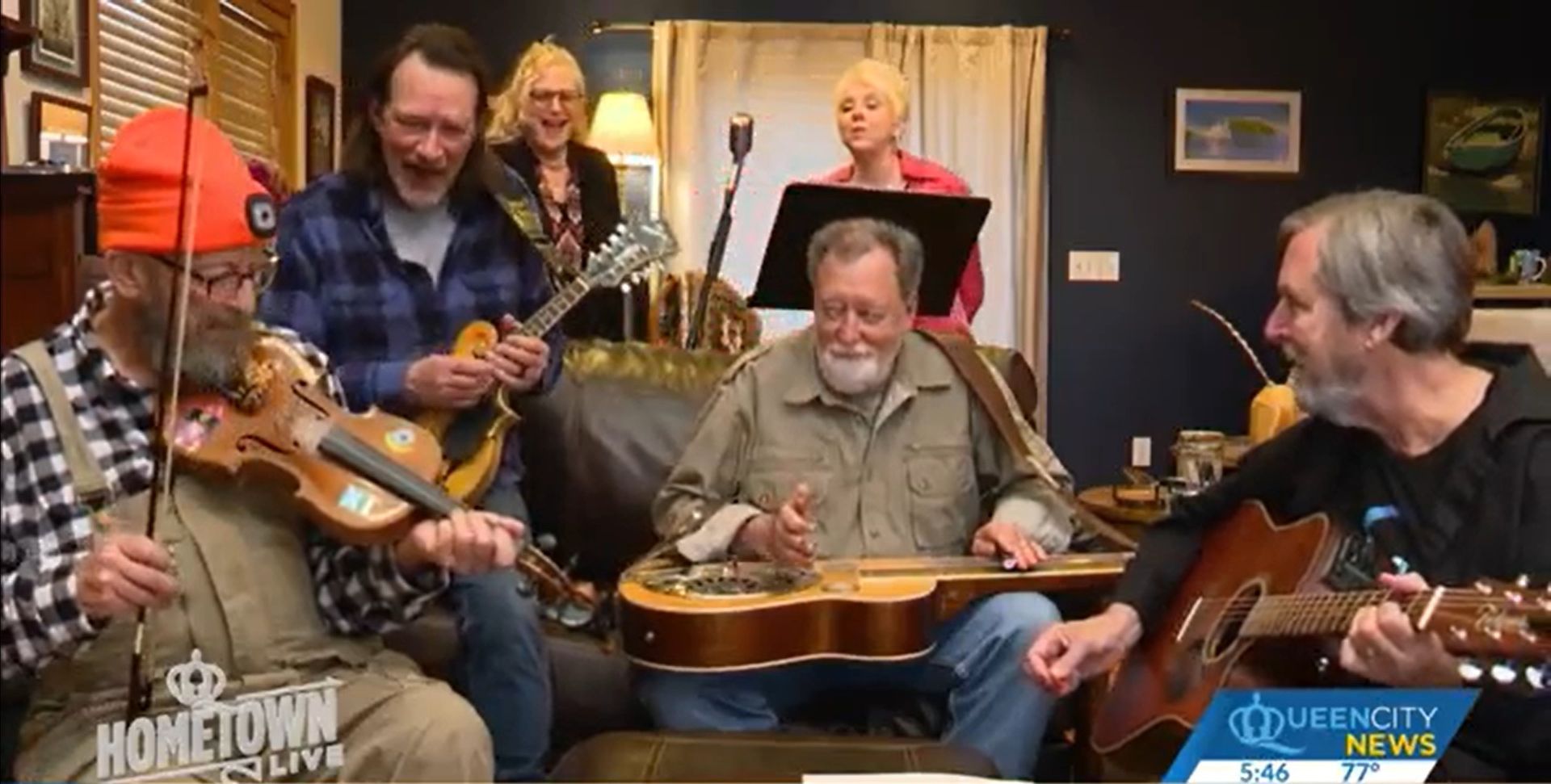 A group of men are playing guitars and violins in a living room.